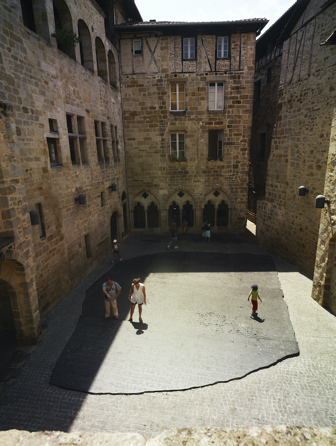 Place des écritures à Figeac : reproduction au sol et agrandissement x 10 de la Pierre de Rosette avec les 3 écritures gravées : hiéroglyphe, démotique, grec ancien (oeuvre de Joseph Kossuth)
Autour de la place, maisons médiévales (fenêtres à meneaux, arcades,....)